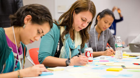 three students working intently on a project involving post-it notes