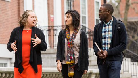 Three people walking and talking, the person on the far left is saying something while the other two on the right are listening and engaging
