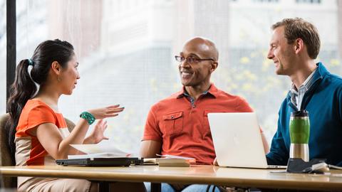 three smiling people talking and sharing ideas while sitting at a table