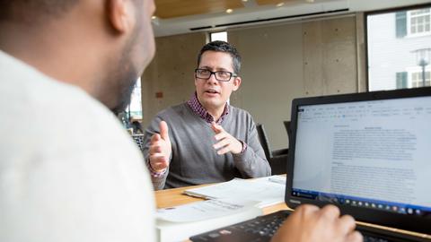 a person talking with another person working on a compter