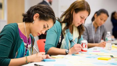 People sitting a a long table writing on multicolored post-it-notes
