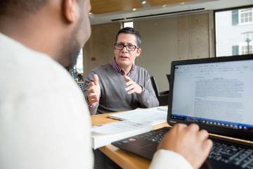 a person talking with another person working on a compter